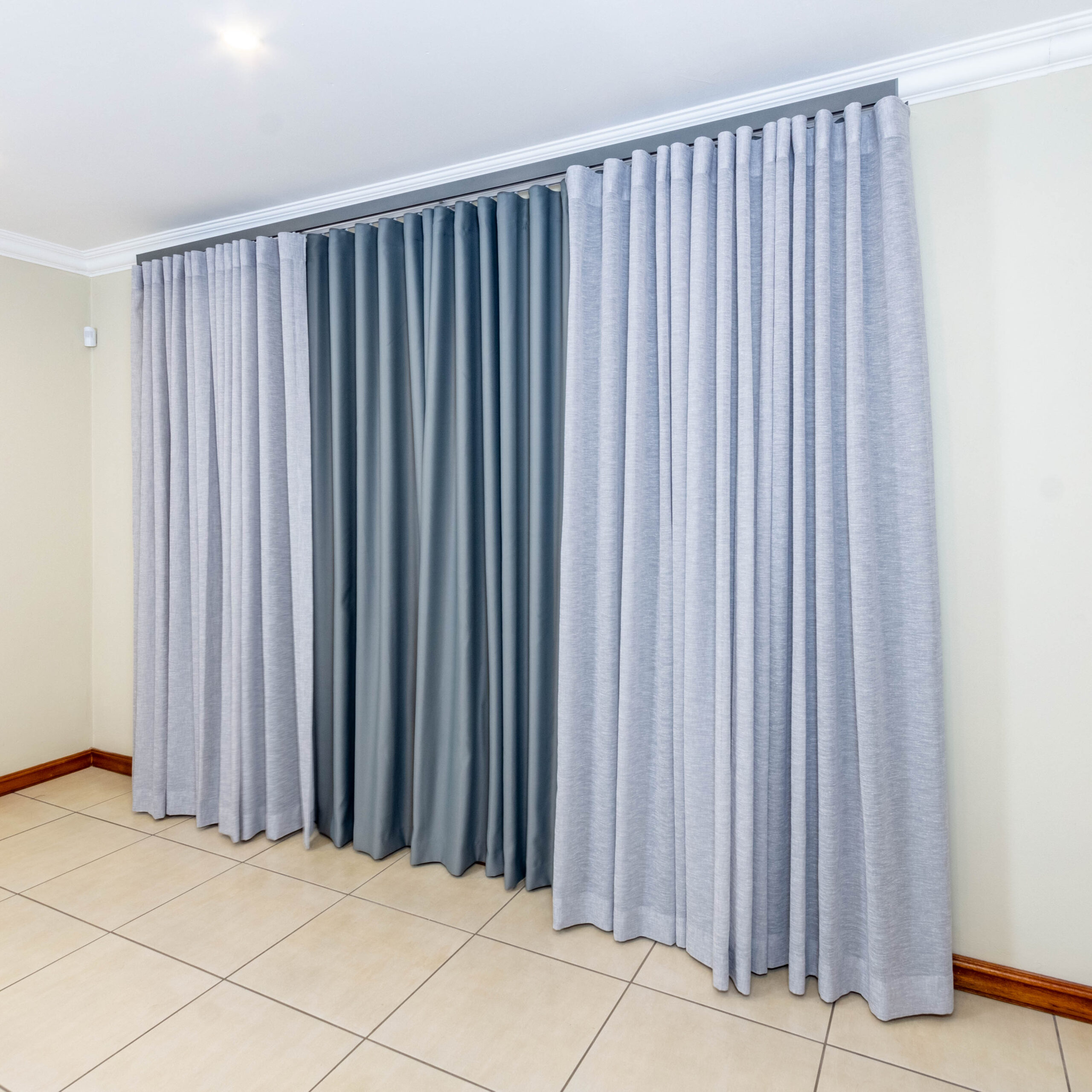 A window with partially drawn thick curtains revealing a layered sheer curtain inside.