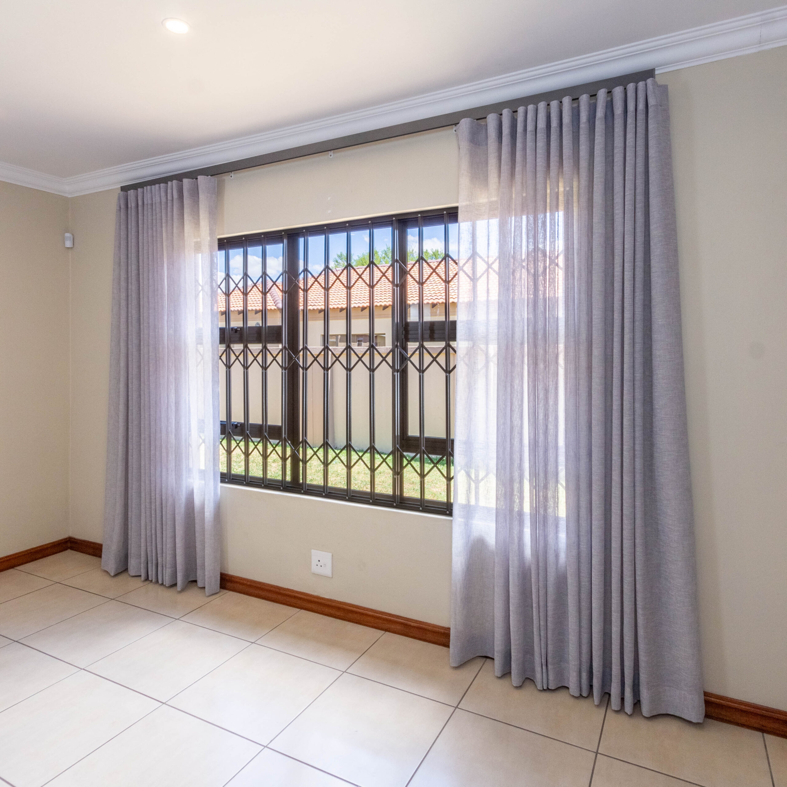 A window with thick gray curtains pulled apart, revealing the window and security bars.